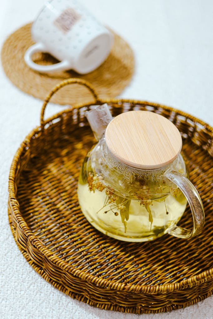 A glass teapot with herbal tea on a woven tray, offering a cozy indoor setting.