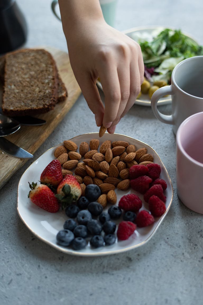 Hand reaching for almonds on a plate with mixed berries for a healthy breakfast.