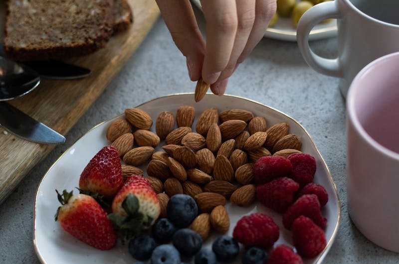Hand reaching for almonds on a plate with mixed berries for a healthy breakfast.